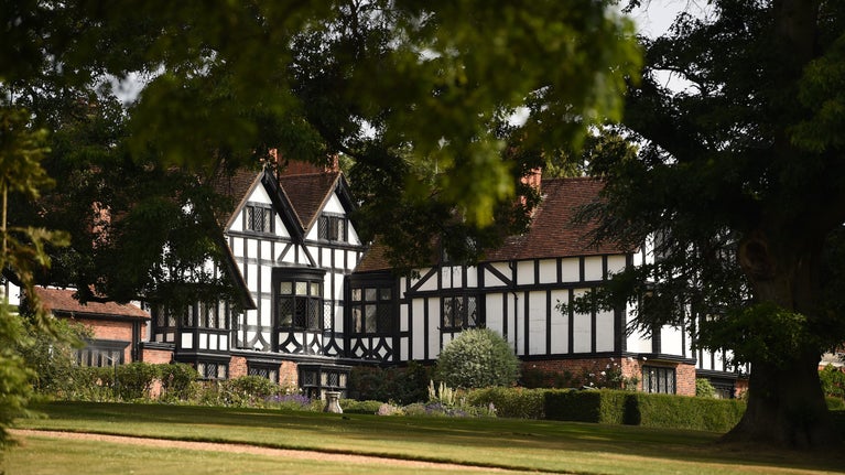 View of the black and white, half-timbered house across the lawn, with large trees to the side, at Ascott, Buckinghamshire
